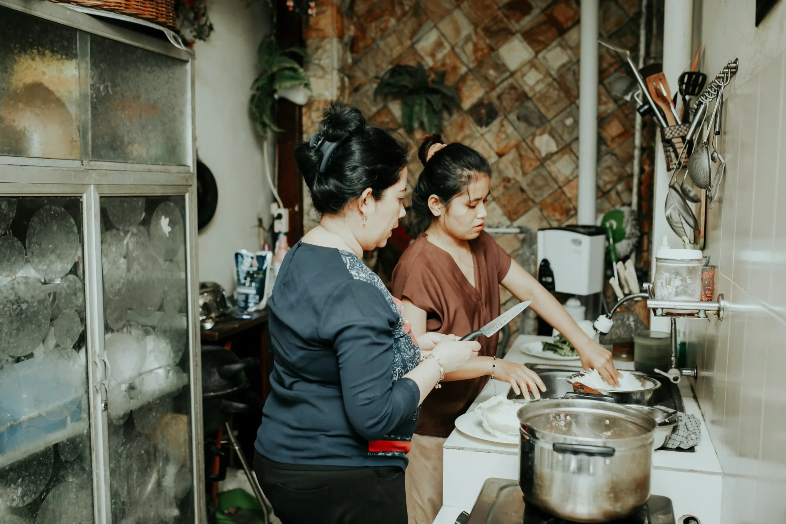 asian mother watching daughter cooking in domestic kitchen